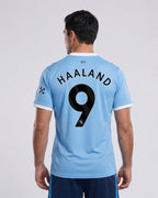 Person wearing a light blue sports jersey with 'Haaland 9' printed on the back, on a plain background.