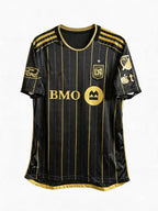 Black sports jersey with gold accents and branding on a white background